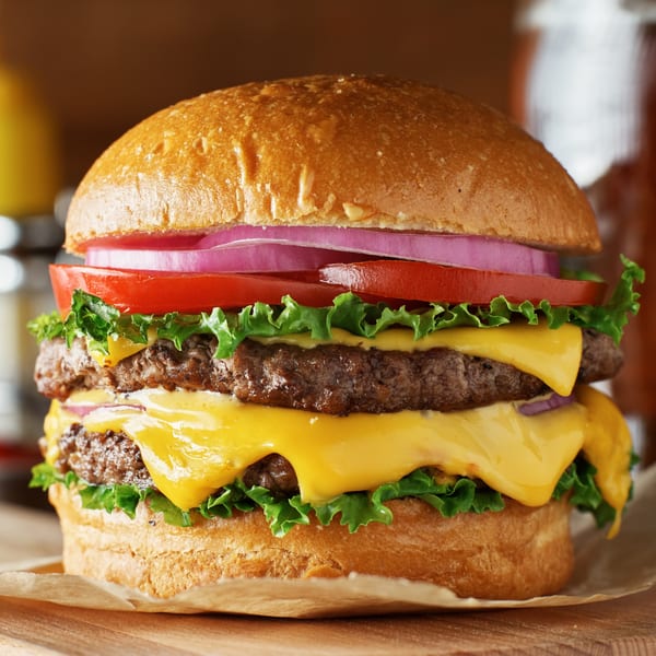 A large double cheeseburger with lettuce, tomato, and red onion on a bun.