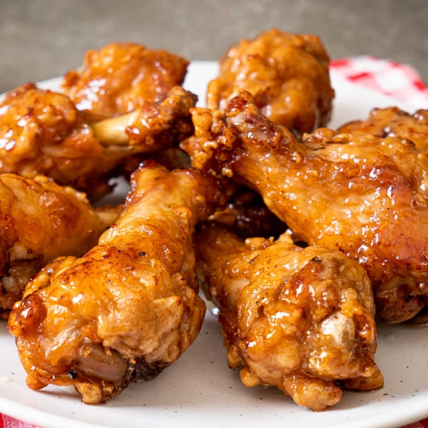 A close-up of several Milan's Pizza glazed chicken drumsticks on a white plate with a red checkered napkin.