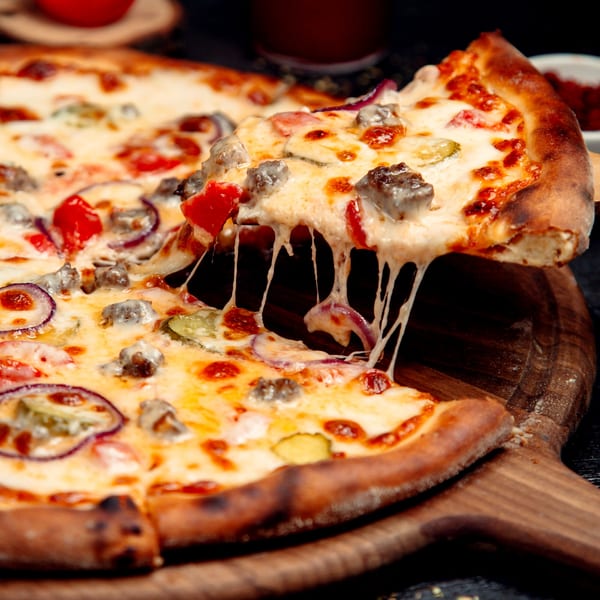 A slice of Milan's Pizza with melted cheese, meat, red onion, and pickles being lifted from the pie.